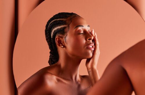 Mulher negra, em frente a espelho, de olhos fechados e tocando a própria face.